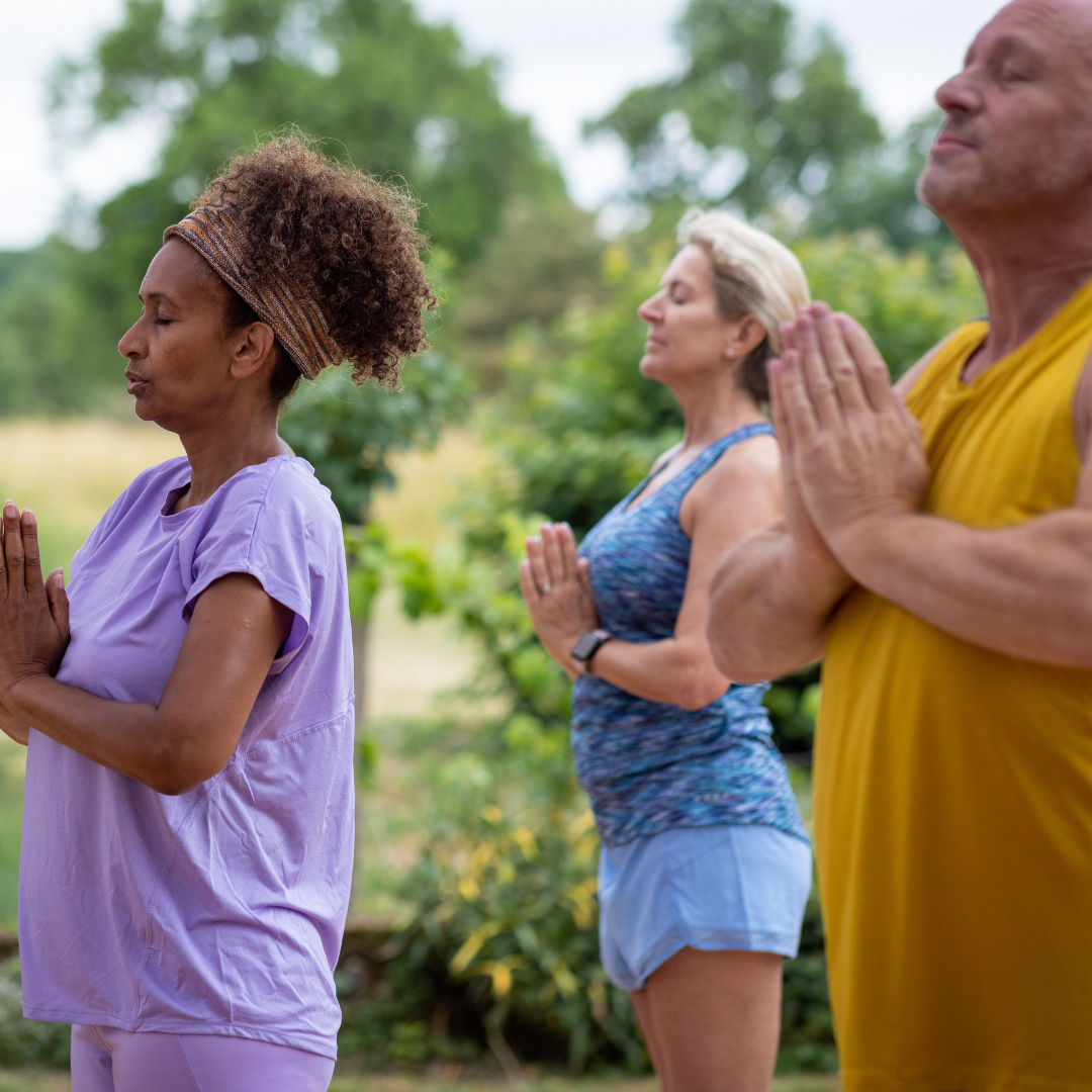 Three people in prayer pose practicing yoga outdoors